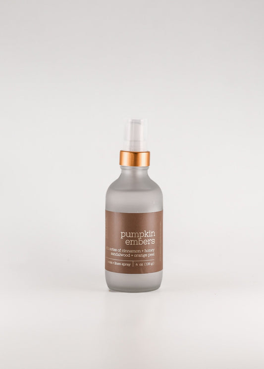 A frosted glass pump bottle of pumpkin embers room spray with a metallic copper collar and a brown label, set against a seamless light gray background. Handcrafted by Sweet Aurora Soap & Candle in New Jersey