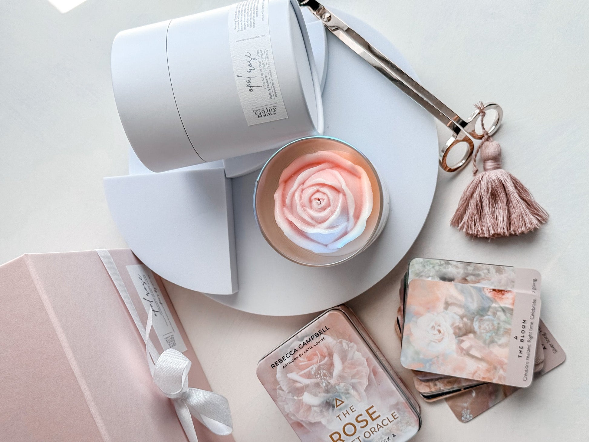 Rose-shaped candle in a white container with packaging and tools on a light surface