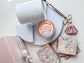 Rose-shaped candle in a white container with packaging and tools on a light surface