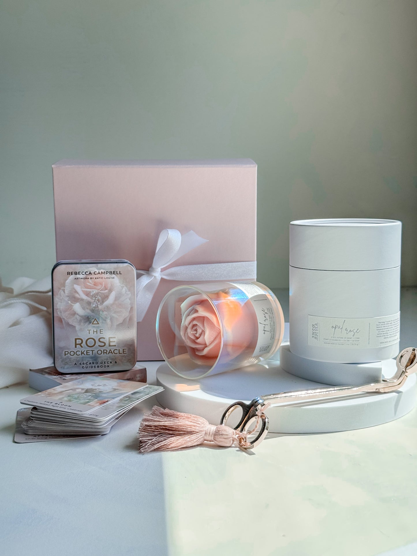 Set of beauty products including a candle, cards, and a small box on a light surface with a neutral background.
