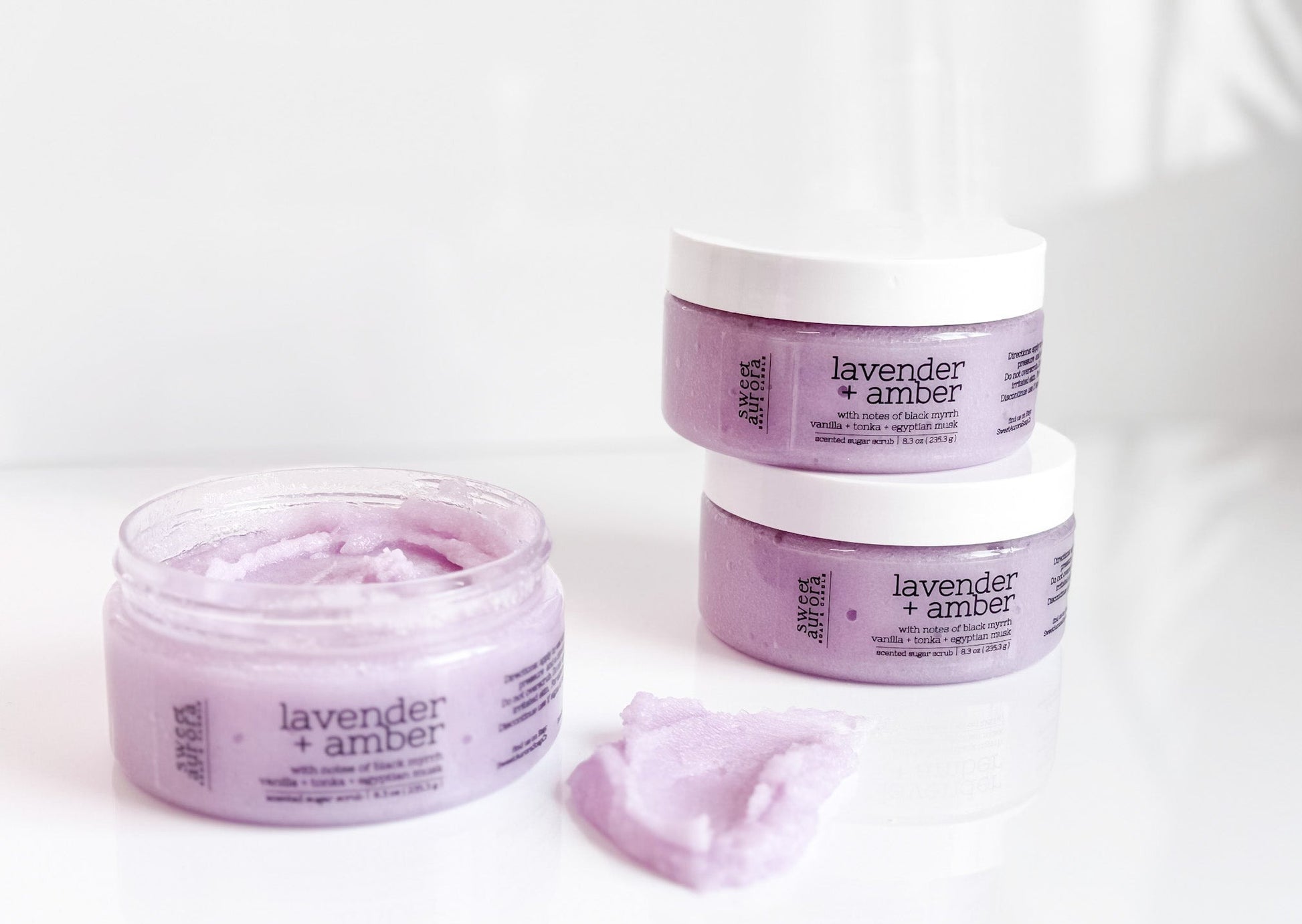 Lavender + Amber sugar scrub jars with open jar showing exfoliating texture